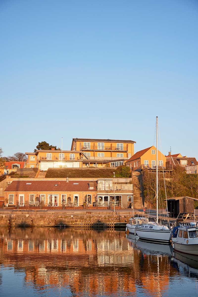 Hotel Kysten set fra Hasle Havn med lystbåde og spejling af hotellet i vandet