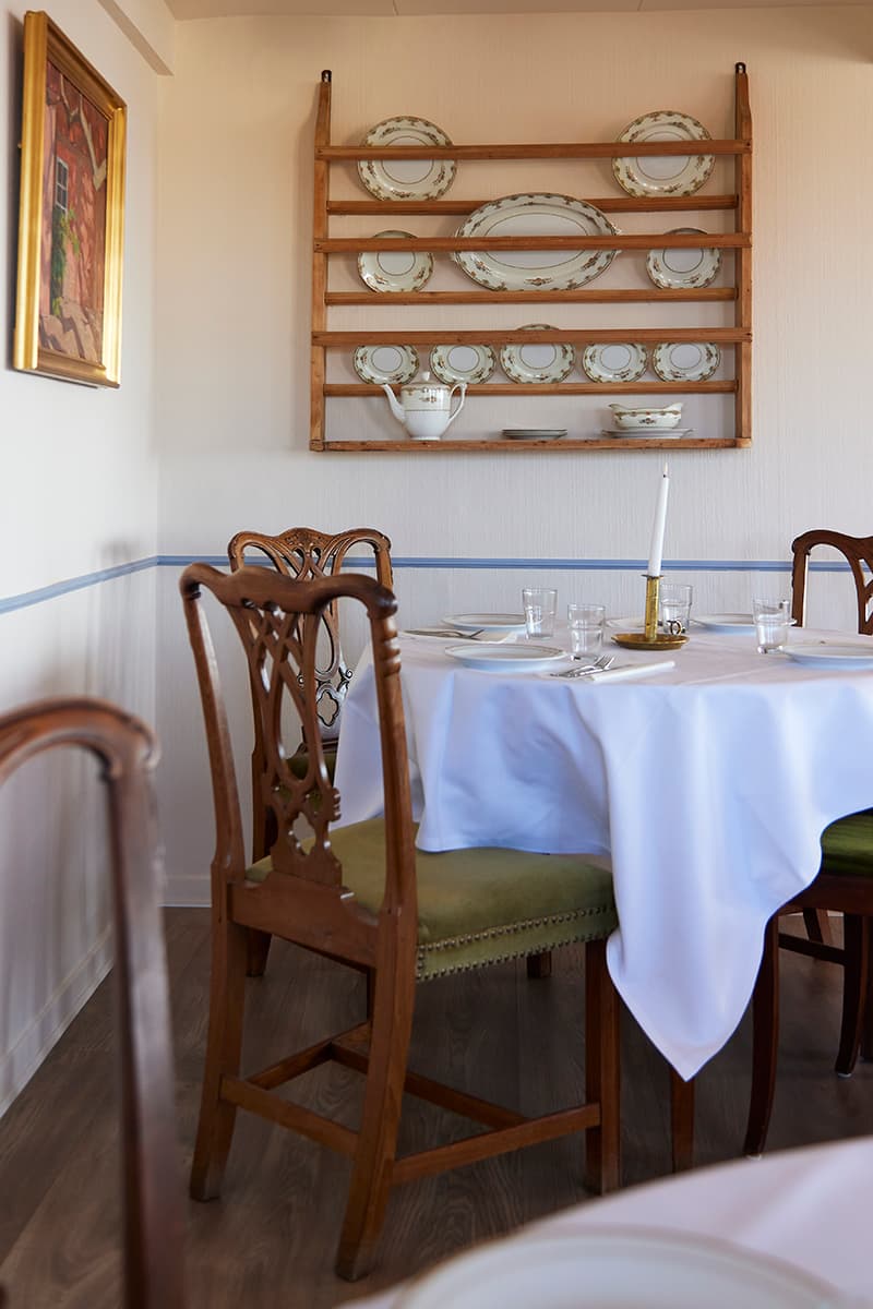 Morgenmad på Kysten Restaurant Bornholm med hvide duge antikke møbler og tallerkenrække
