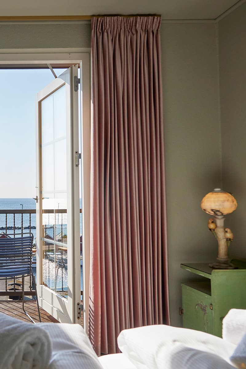 Værelse på hotel på Bornholm med havudsigt stol på terrasse grønt natbord med lampe gardiner og seng