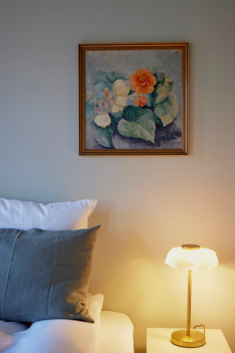 Dobbeltværelse seng med puder natbord lampe og maleri på væg